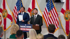 Two men in suit and ties by podium that reads "Taking Down Voter Fraud." A bunch of flags are behind them 