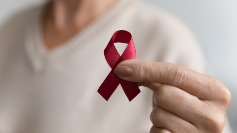 A hand holds up a red ribbon as an HIV or AIDS awareness symbol