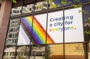 A picture of a banner displayed on the outside facade of City Hall shows the LGBTQ colors on a white background with the words "Creating a city for everyone"