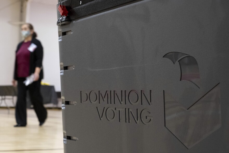 A worker passes a Dominion Voting Systems ballot scanner during Georgia's runoff Senate elections in January in Gwinnett County outside Atlanta. Former President Donald Trump and his allies spread falsehoods about the company's role in the 2020 election, leading to a slew of defamation lawsuits.