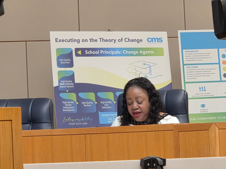 Woman seated at dais in front of chart on easel