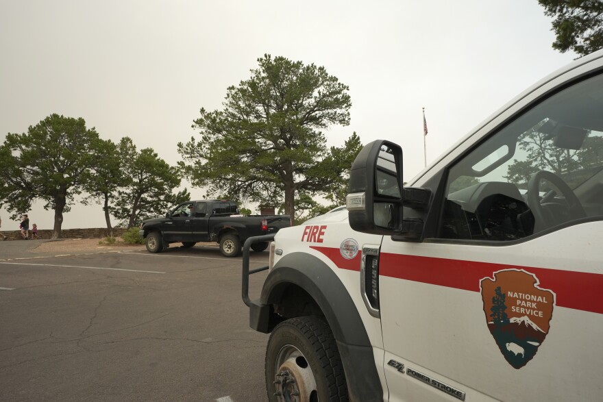 Smoke from the Dragon Bravo Fire moves over the Grand Canyon from the North Rim as a National Park Service fire vehicle sits facing the South Rim, Monday, July 14, 2025, in Grand Canyon National Park, Ariz.