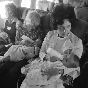Edna Deichl, left, wife of a Free Flight pilot, naps while Linda Reid, center, wife of the co-pilot, and Lillian Bradshaw, an orphanage worker, feed their charges on a flight from Seattle to Chicago, bringing Vietnamese orphans to their new homes, April 6, 1975.