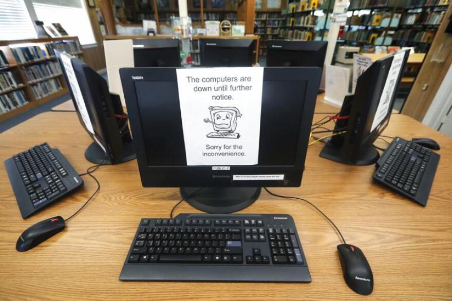 A bank of computers in a semicircle are off and have a sign taped to the screen saying "The computers are down until further notice."