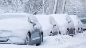 Parked cars along a city street covered in snow after a snowfall.