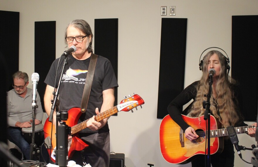 Chris Petrack is in the background playing a hand drum. Rich Mattson in the middle playing guitar and singing. Germaine Gemberling is on the right playing guitar and also singing. 