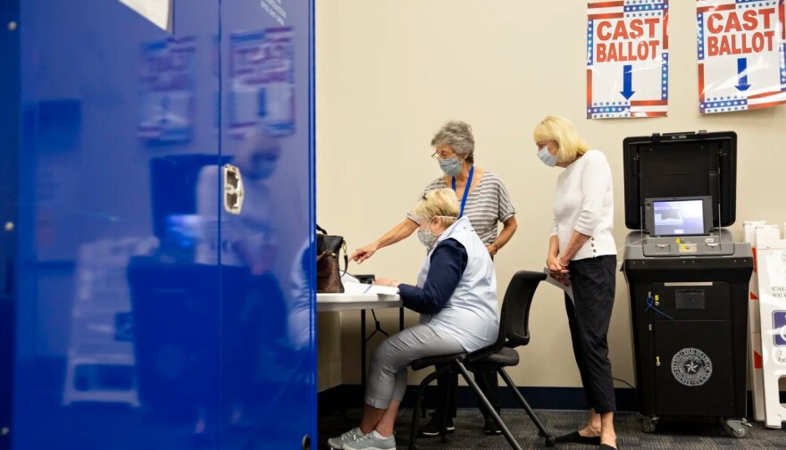 Poll workers help a voter in a voting booth