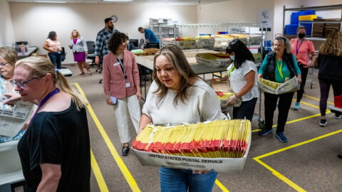 Workers handling U.S. Postal Service trays full of ballots.