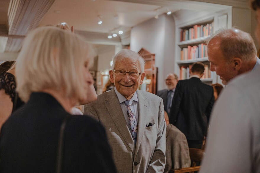 An elderly couple smiles as they meet with a younger man at an event.