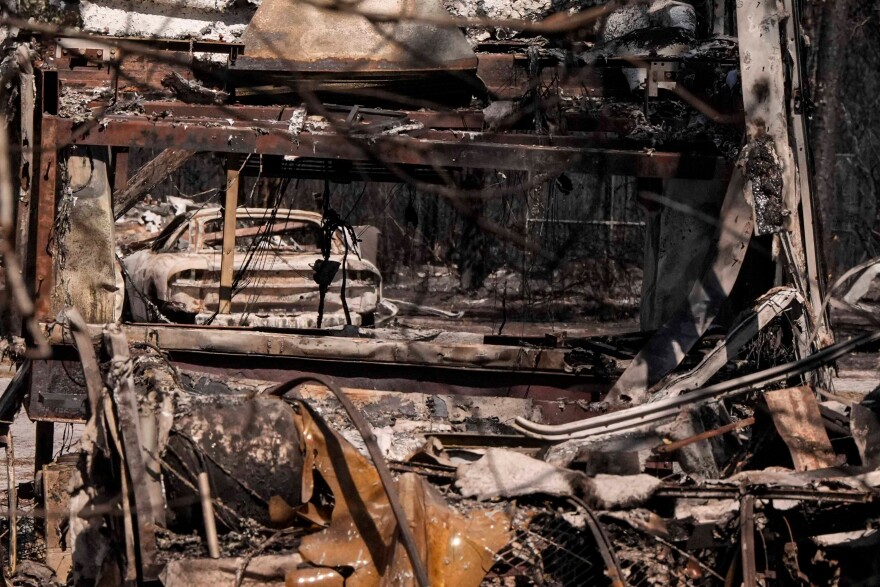 A burned vehicle sits near a destroyed home, foreground, as the Brantley Highway 82 fire burns, Thursday, April 23, 2026, near Nahunta, Ga. (AP Photo/Mike Stewart)