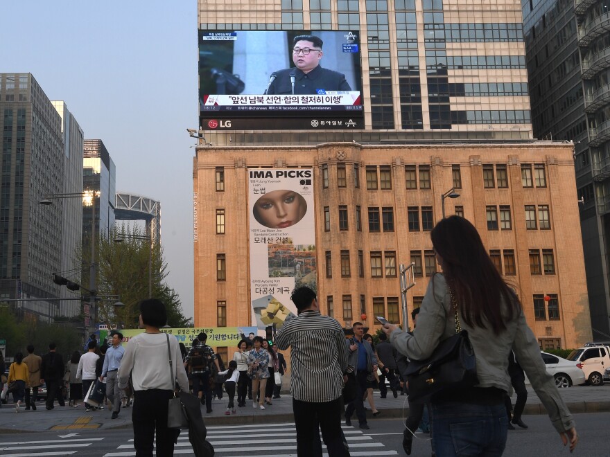 Pedestrians in downtown Seoul, South Korea, walk across the road as a big screen shows live footage of a joint news conference with Kim and Moon during the Inter-Korean Summit.