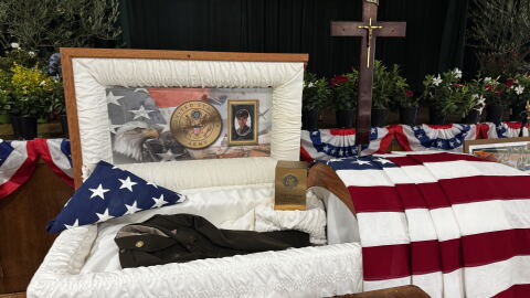 Casket with photos of Sgt. Adolph Aguirre and his uniform. American flag draped over. 