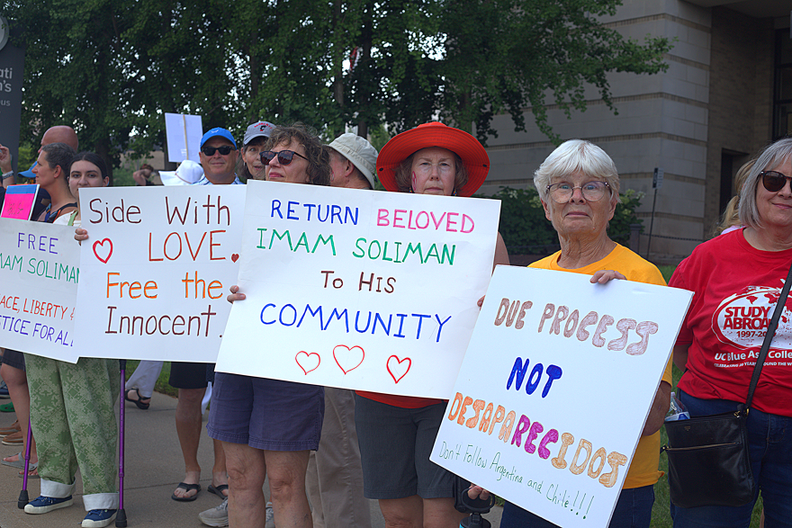 A line of people holding signs with messages like "return beloved imam Soliman to his community"