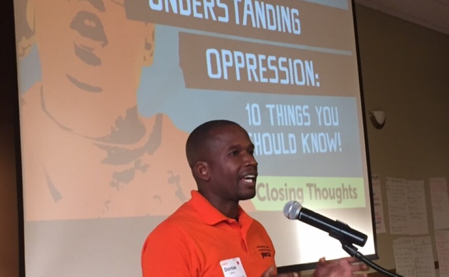 Man at a microphone with screen behind him that reads, "Understanding Opresssion: 10 Things You Should Know"