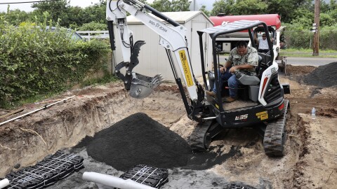 Contractor Wendall Bandmann drives an excavator helping to install a leach field, which is connected to a septic tank, to replace a residential cesspool, May 11, 2023, in Waialua, Hawaiʻi.
