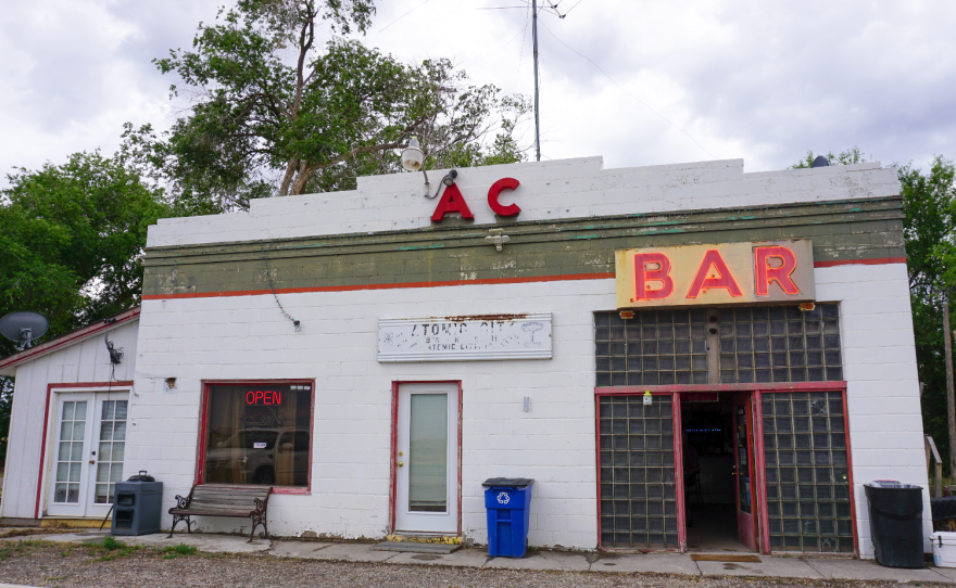Front view of a slightly rundown building with two large signs that say "AC" and "BAR" with a smaller, mostly-faded one that says, in part, "Atomic City."