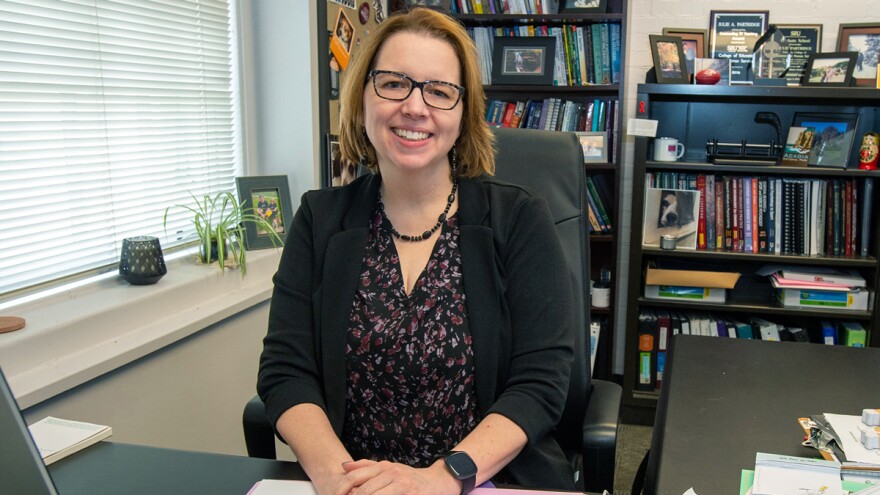  Julie Partridge sits at her office desk in front of a wall of bookshelves