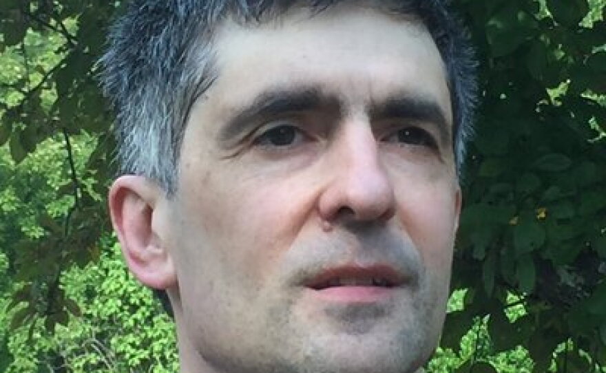 A man with short grey hair, wearing a blue polo shirt