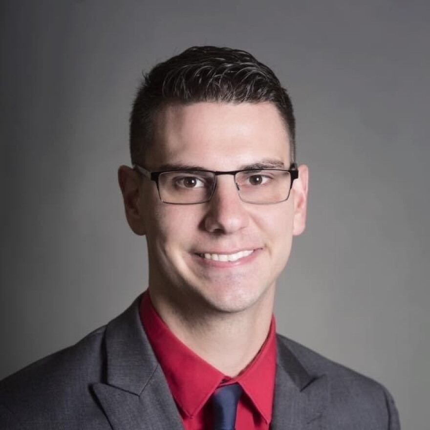 Closeup of young man smiling and wearing a dark suit and tie with a red shirt