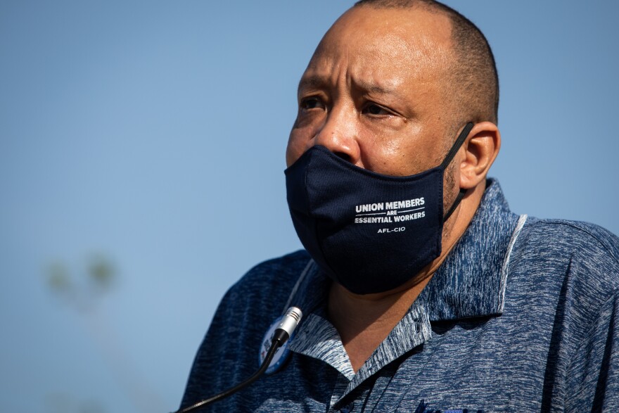 Brent Payne, of the Amalgamated Transit Union, speaks at a podium in 2020 outside the Delco Activity Center. Payne is wearing a face mask that says, "Union members are essential workers. AFL-CIO."
