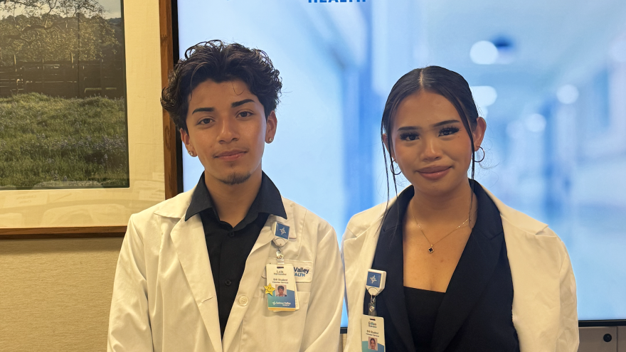 Two students in white lab coats with hospital badges pose for the camera. 