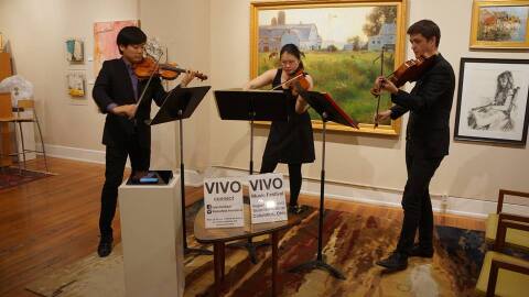 color photogaph of violinists Siwoo Kim and Alicia Hui, and violist jack Stulz standing up and playing chamber music at a Short North art gallery