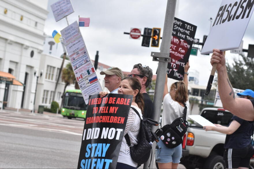 People stand along South Orange Avenue in downtown Orlando on Saturday, holding signs as passing drivers honk in response during the No Kings Day rally.