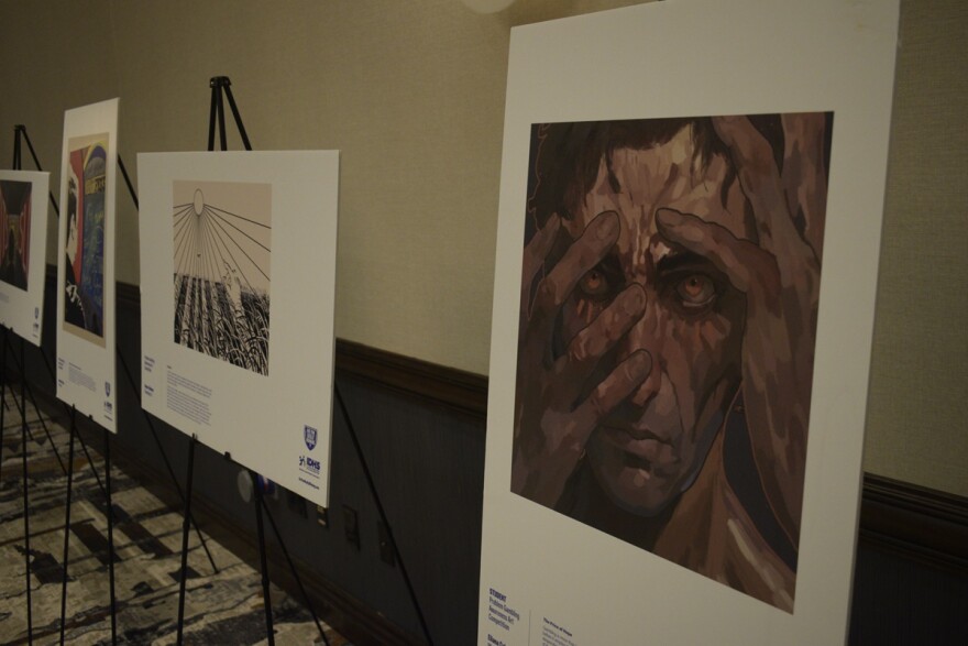 A painting of a hand partially covering a man's face as the painting hangs in a conference center display next to a row of other pieces of artwork