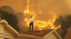 Standing on a rooftop, a man looks at the Springs fire's approaching flames in California Friday. The wildfire, reportedly, 20 percent contained, might be weakened by high humidity and cooler temperatures Saturday.