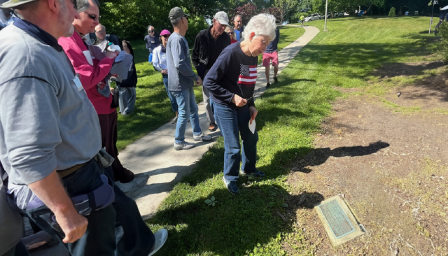 woman in flag sweater looks at a plaque on the ground