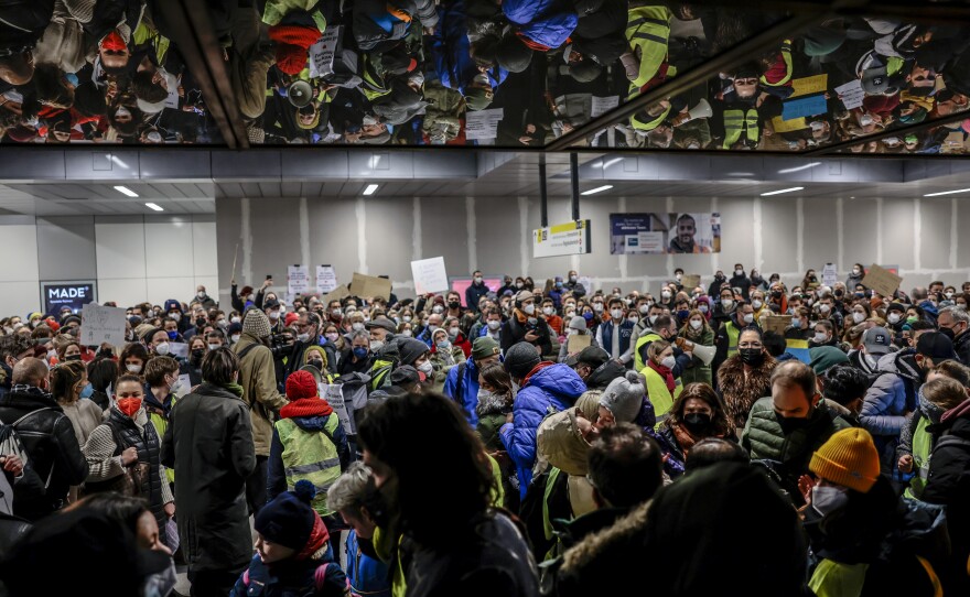 Hundreds of people crowd in large room at the station, some holding signs, others wearing volunteer vests.