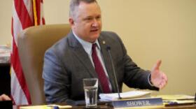 white man in a suit speaks from a desk