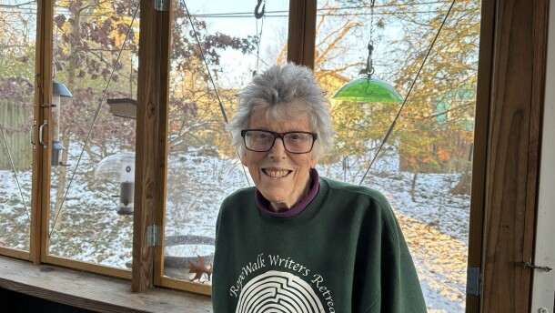Antonia Matthew standing in front of a bank of windows looking out on a snowy yard with bird feeders visible close to the window.