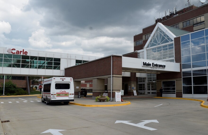 The main entrance of Carle BroMenn Medical Center showing a small passenger van parked outside and an enclosed walkway above adorned with a logo that reads 'Carle.'