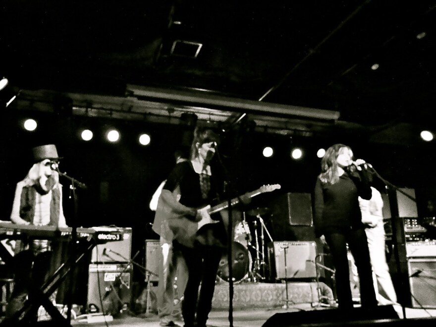 A black-and-white photo of three musicians on a stage playing in a band