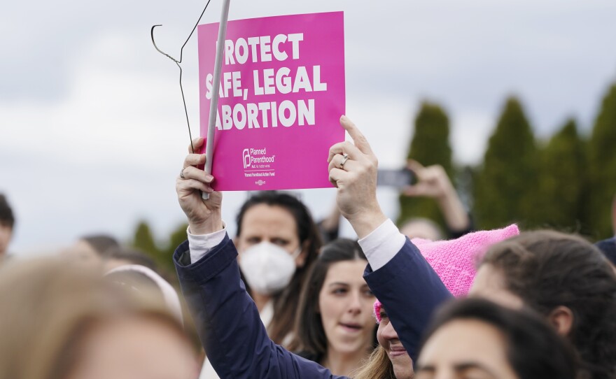 A person holds a sign that reads "Protect Safe, Legal Abortion" next to a coat hanger, Tuesday, May 3, 2022, during a rally at a park in Seattle in support of abortion rights. (AP Photo/Ted S. Warren)