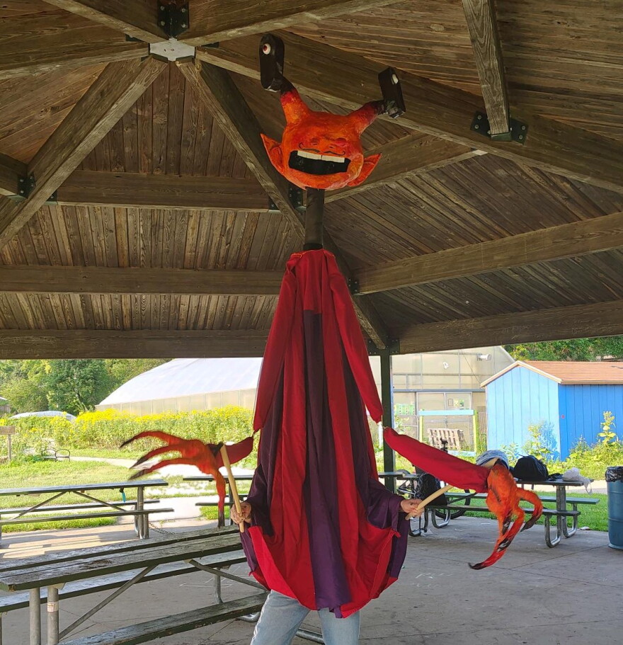 Puppet being operated by a person inside it, it has a devilish face and long fingers
