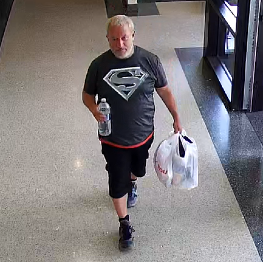 Noam Routtenberg wearing a black Superman t-shirt and shorts while carrying a bottled water in his right hand and a bag in the left hand
