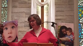 Woman at church podium holding a photo of children in each hand.