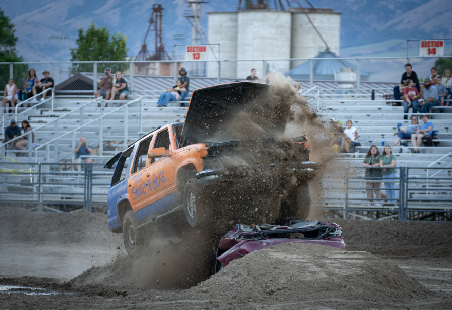 A car goes up over an obstacle, the hood up and dirt flying everywhere. 