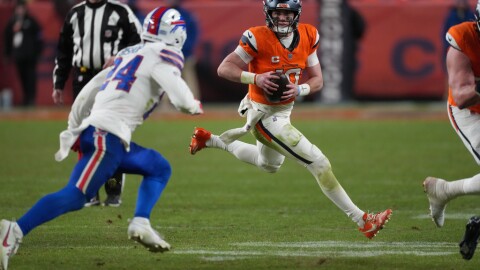 A football player in an orange jersey runs with the ball from an opposing player in a white jersey.