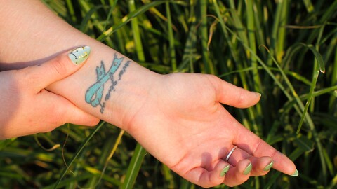 S., a 25-year-old from Clarkston, shows a tattoo she got that says “never give up.” She got the tattoo in 2017 to represent her battle with PTSD, which has affected her mental health for years. The tattered but still-whole blue ribbon represents that even though her experiences left her with trauma, she is still alive. S. says that after surviving her “worst” suicide attempt roughly seven years ago, the tattoo means more to her than ever: “Even though my mind had given up, my body continued to fight for me,” she says. (Credit: Rachel Sun/NWPB)