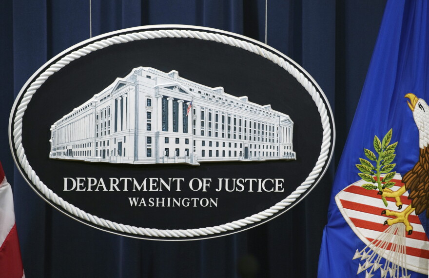 The oval seal of the Department of Justice, which shows an illustration of the DOJ building in a three quarter view on a dark background