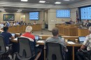 A horse shoe of county board members sit facing a large desk. 