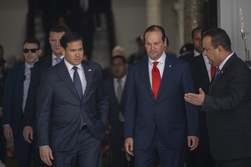 Marco Rubio (right) walks next to a man in a blue suit and red tie. 