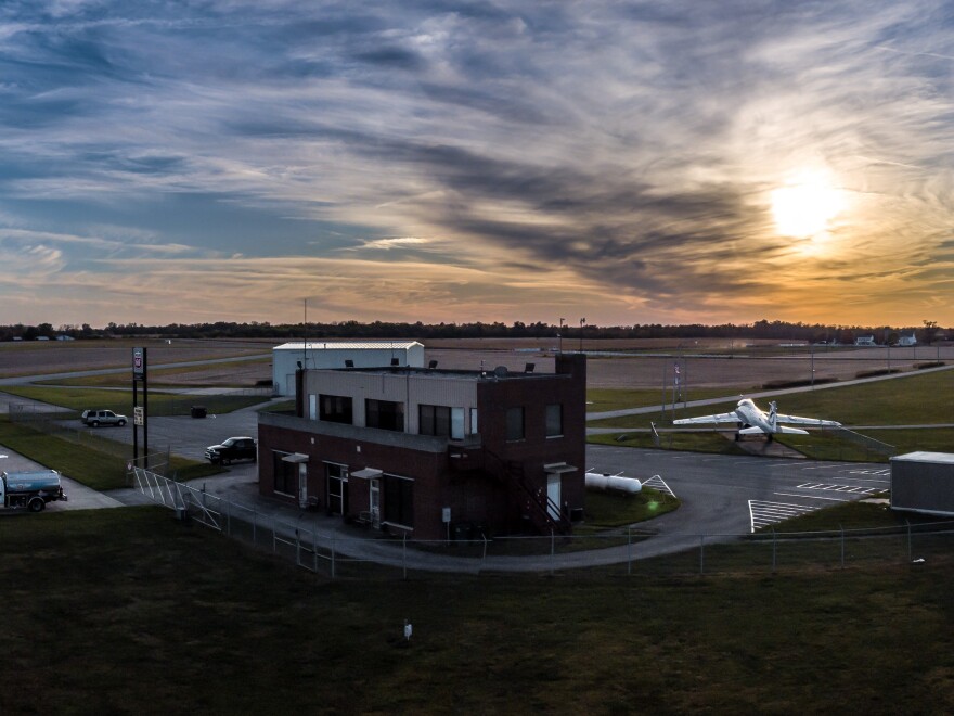 a small airport building with a plane as the sun glows in a cloudy sky
