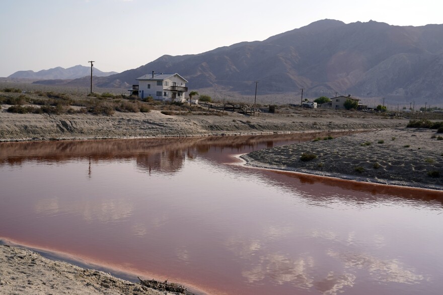 Clouds and nearby mountains are reflected in a polluted canal.
