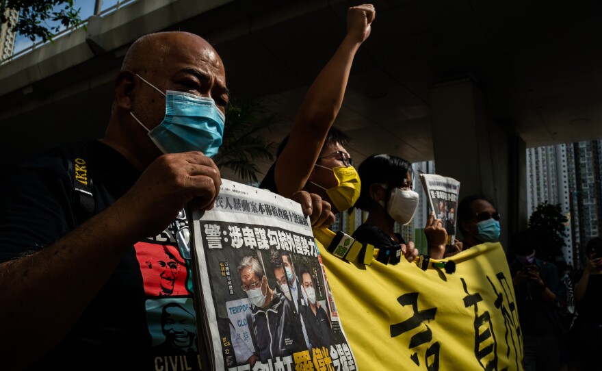 People in masks hold newspapers and a banner while protesting.
