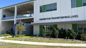 A photo of the facade of a building and a small garden out front. A sign on the building says "Center for Transforming Lives."