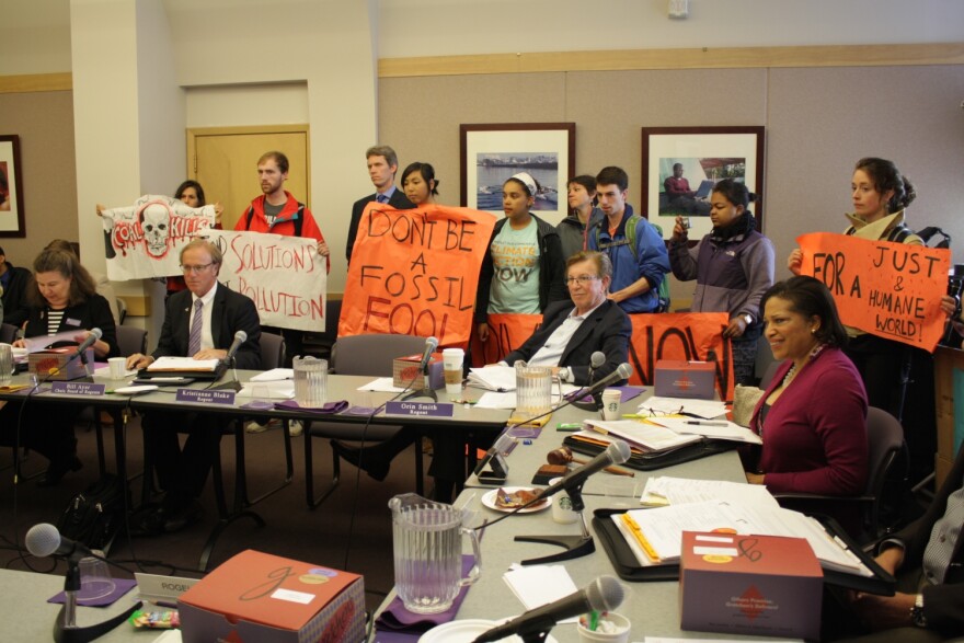 Protesters hold signs around a table populated by UW Regents.
